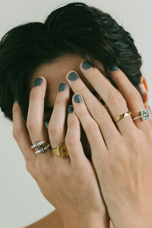 Photo of a man with rings and painted nails, covering his face.